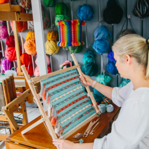 Image of a woman holding a weaving loom with a blue and red textile on it