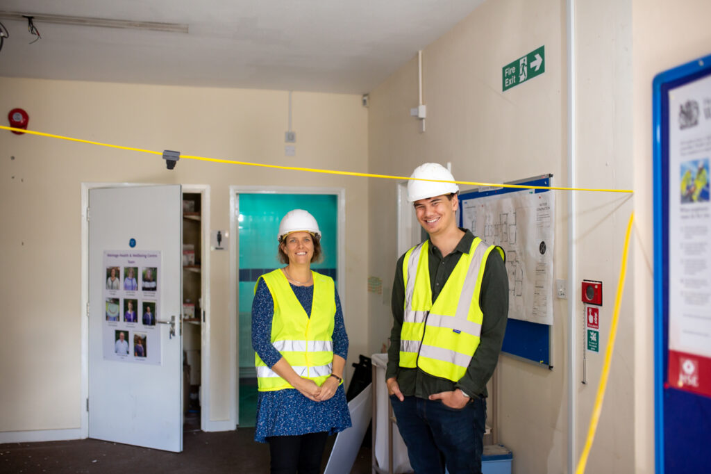 Two members of the Makespace Oxford Team pose in a room, wearing high visibility vests and white hard hats