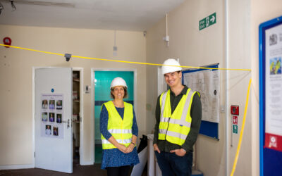 Two members of the Makespace Oxford Team pose in a room, wearing high visibility vests and white hard hats