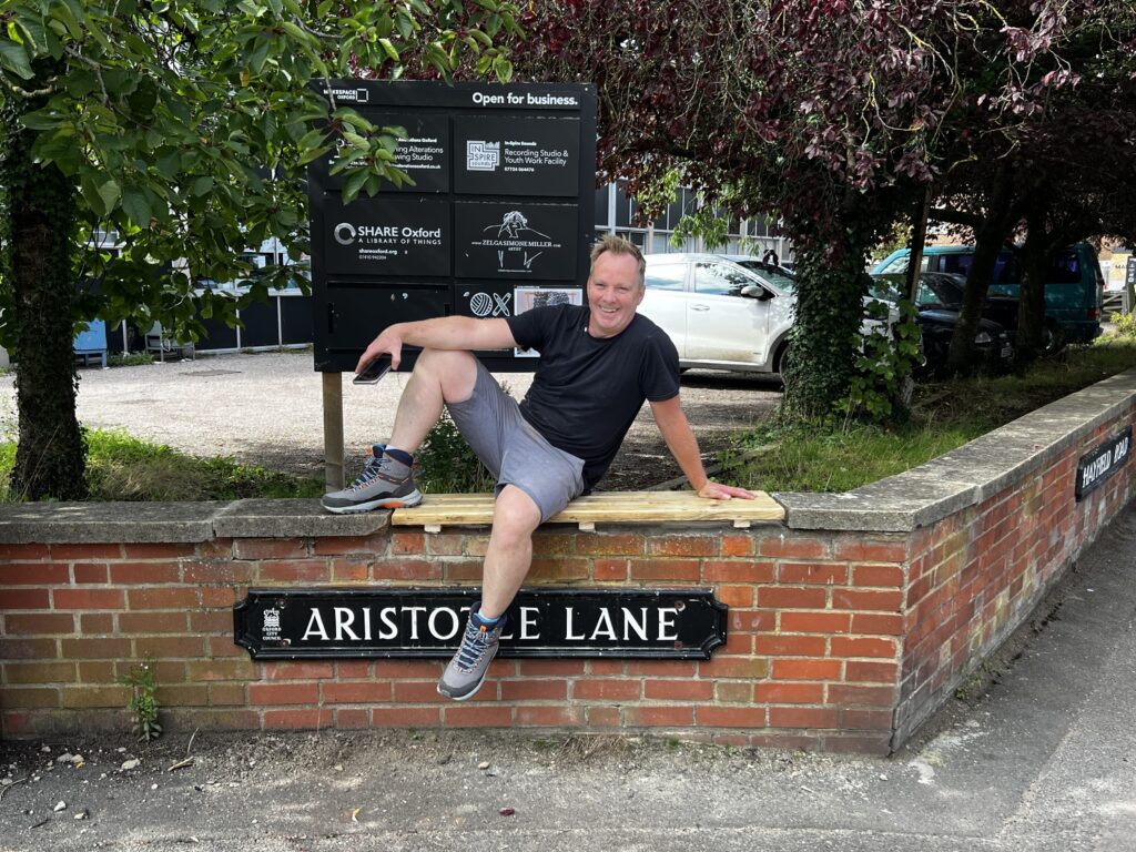 Facilities coordinator, David, sitting on new wooden bench on the Aristotle Lane wall