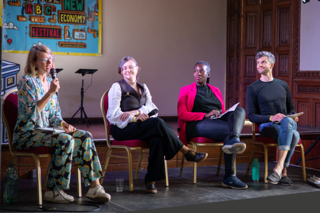 Panel of four people on stage at Stir to Action festival: Bex Trevalyan with mic in hand, Kathryn Chiswell Jones, Juliet Can and Andy Edwards