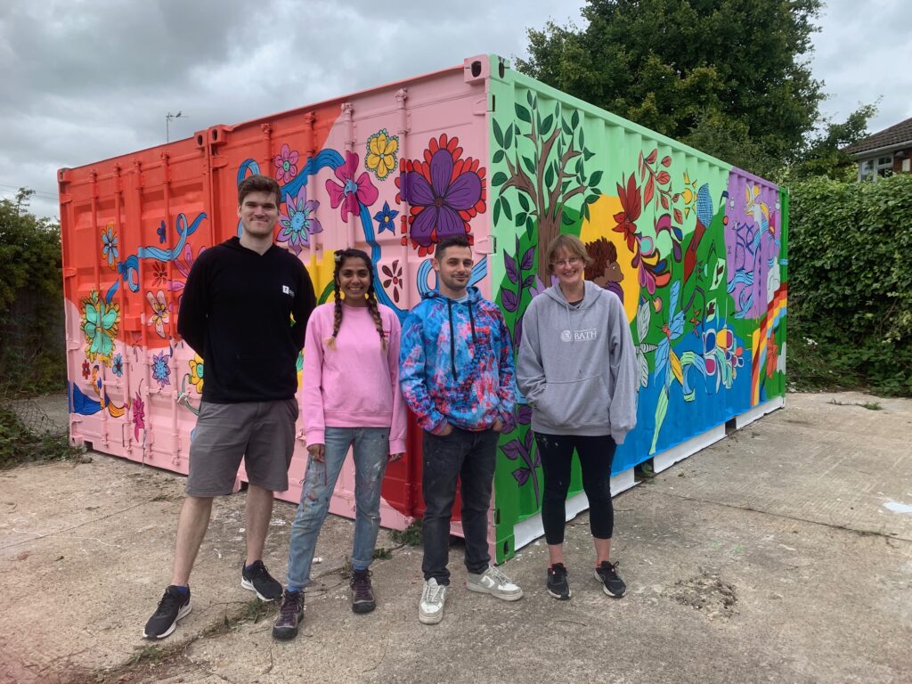 Ride Revolution Bike Lock Pictured with support artist Tom Mclean, lead artist Saroj Patel, support artists Jordan Vanderhyde and Sarah Keenan; standing in front of a shipping container covered in a colourful mural featuring flowers, shapes and bright colours