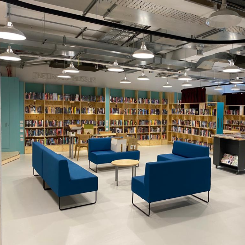 A room fitted with bookshelves on the wall and a square arrangement of blue sofas
