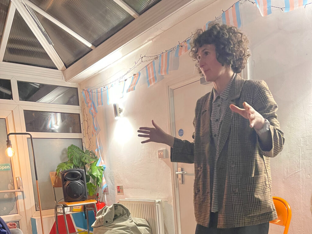 A woman standing facing an audience, talking and gesticulating