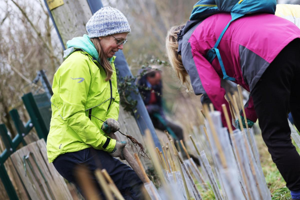 Jo Harvey digging in a garden, wearing a luminous windbreaker and a grey beanie